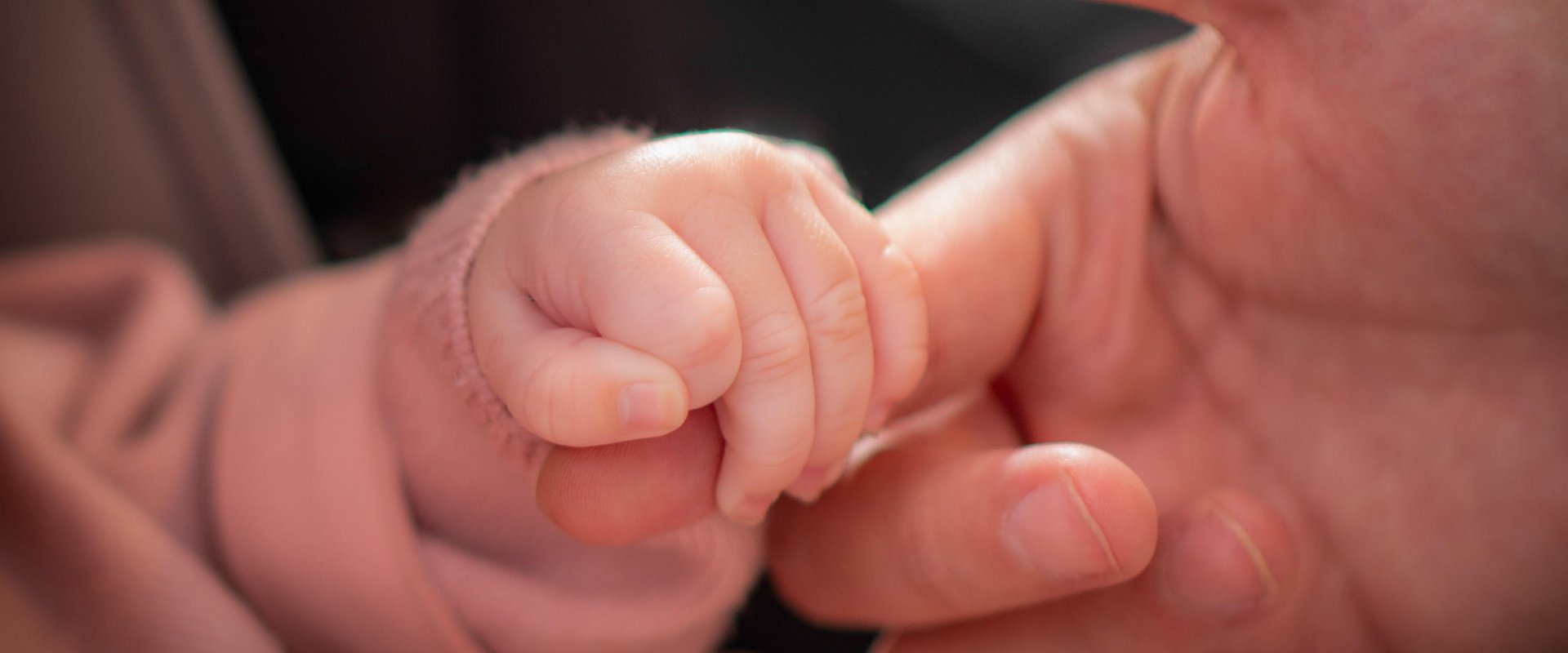 A baby holds an adult's finger in its hand.