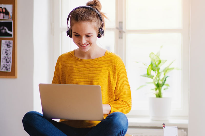 woman sitting using her laptop while wearing headphones