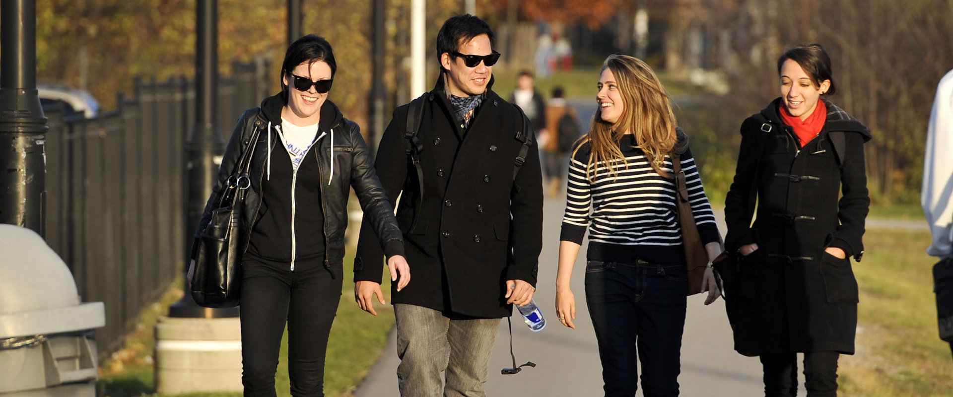 Four students walking on a path at Humber in the fall; trees with coloured leaves can be seen in the background.