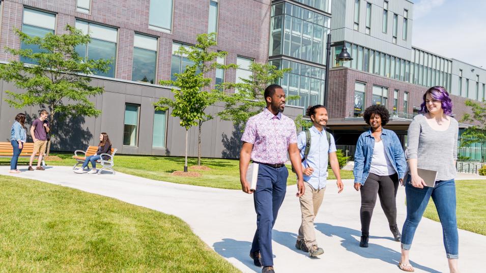 Students walk away from a building on Humber Lakeshore campus down a pathed path lined with grass on a sunny summer day